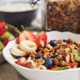 bowls-of-granola-with-yogurt-fruits-and-berries-on-white-surface