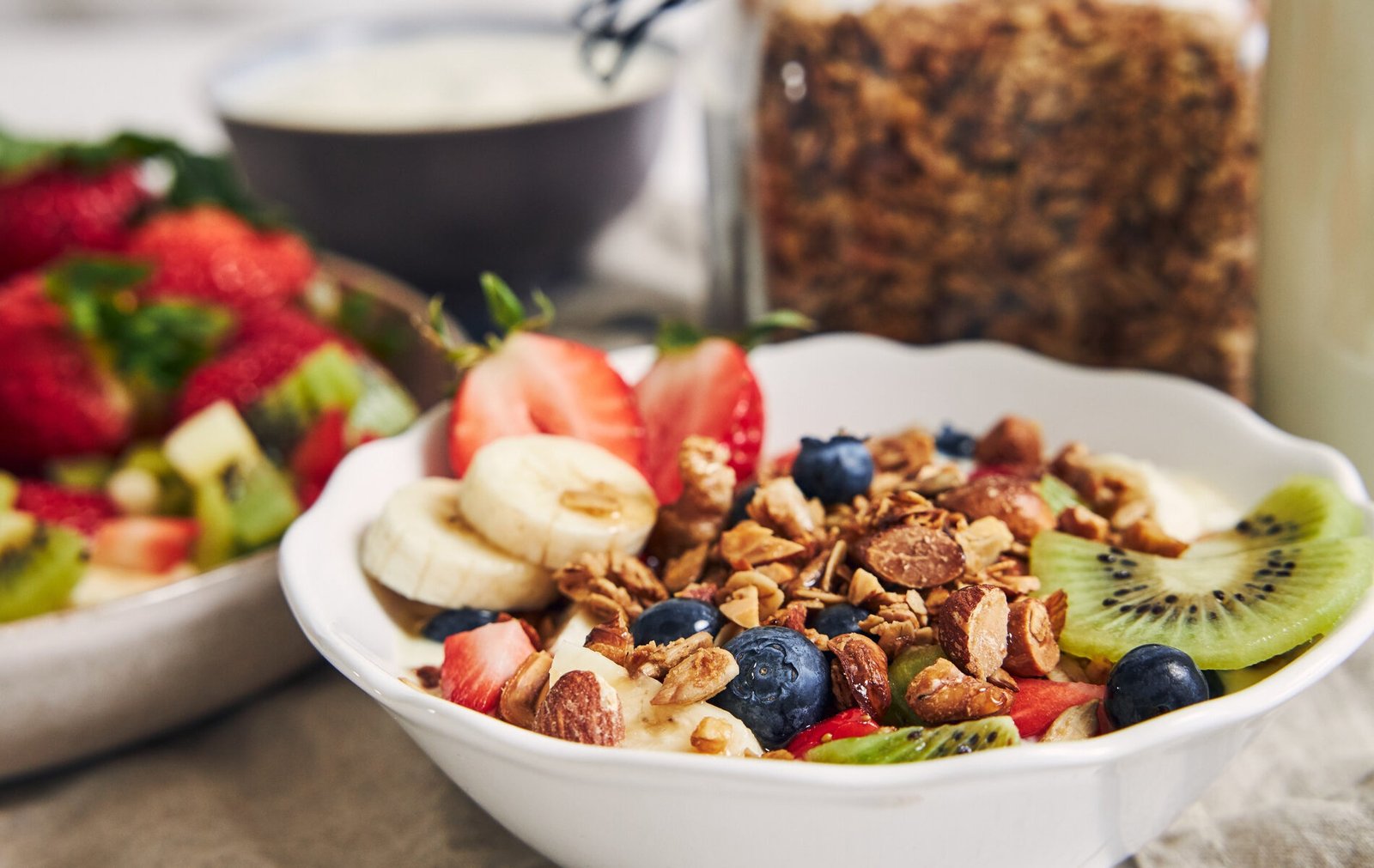 bowls-of-granola-with-yogurt-fruits-and-berries-on-white-surface